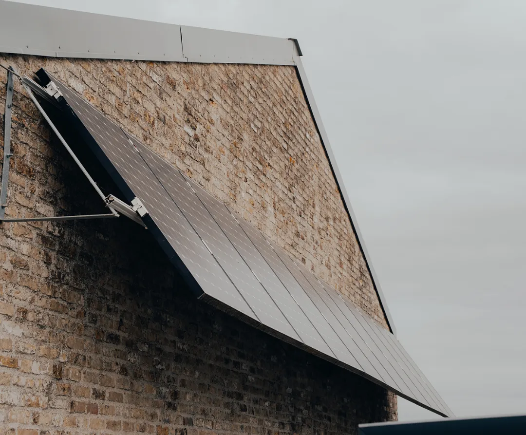 Zonnepanelen gemonteerd aan de bakstenen gevel van een gebouw onder een bewolkte hemel.