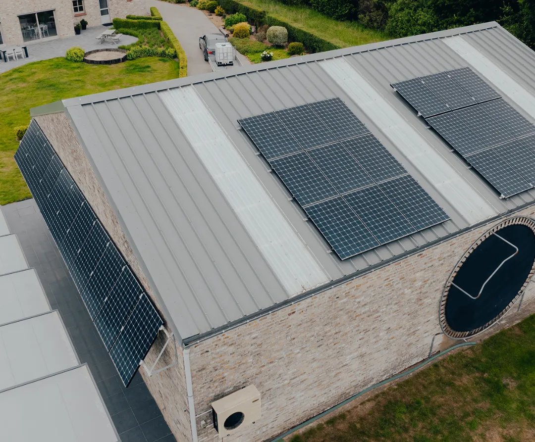 zonnepanelen-bedrijfspand-dak Zonnepanelen gemonteerd aan de bakstenen gevel van een gebouw onder een bewolkte hemel.